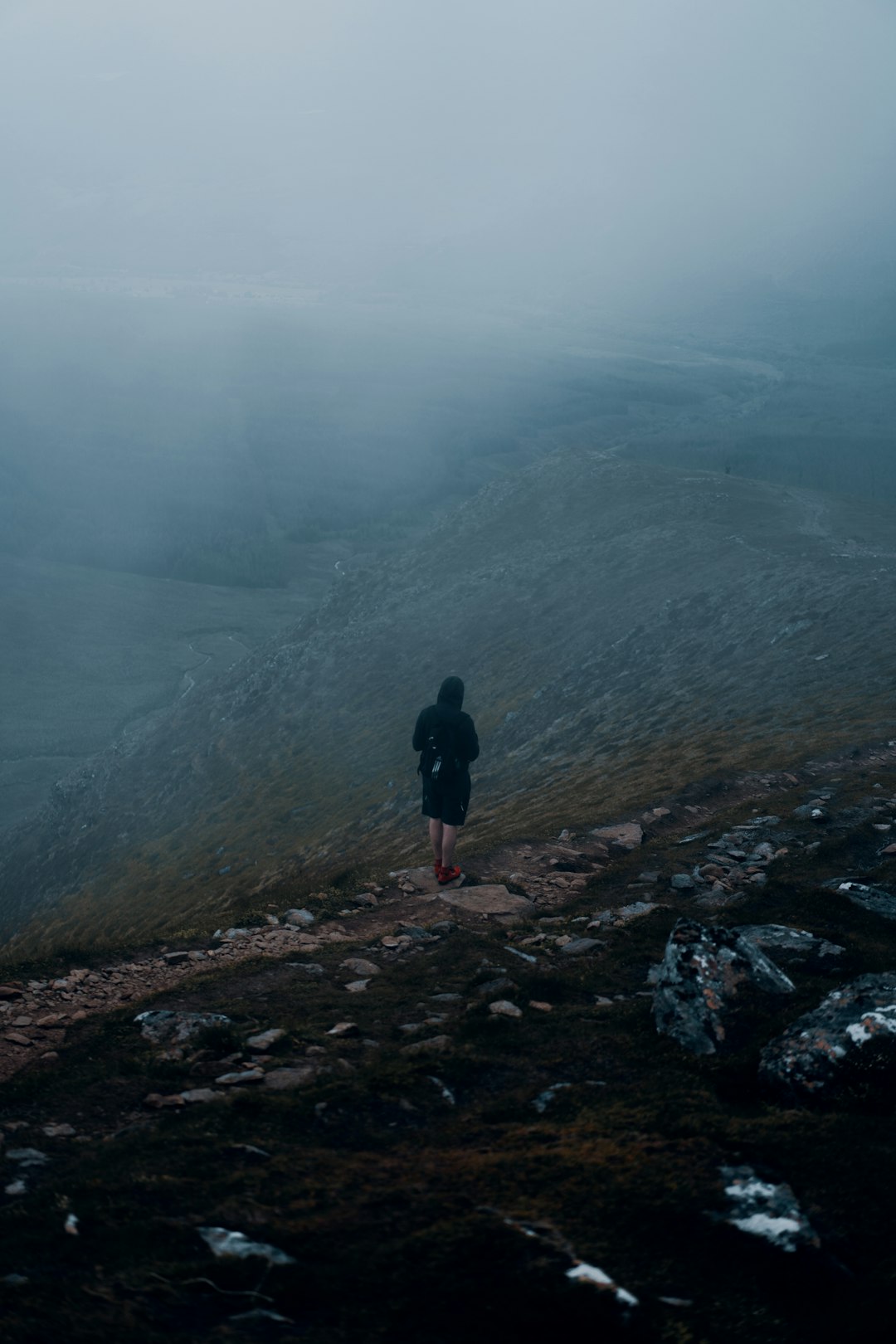 person in black jacket standing on rocky hill during foggy weather