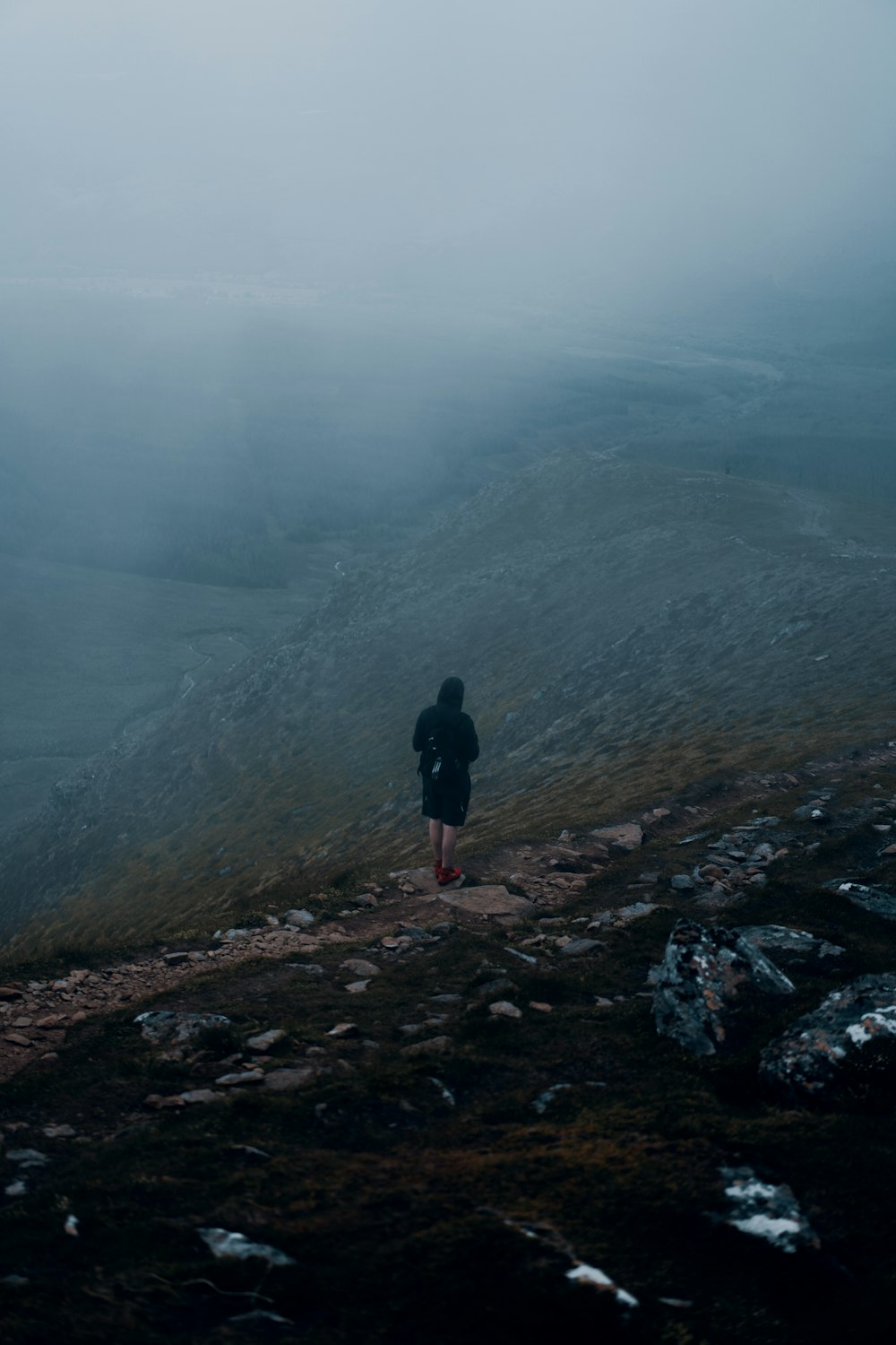 person in black jacket standing on rocky hill during foggy weather