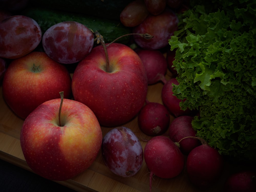 a pile of red apples sitting on top of a wooden cutting board