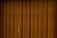 Vertical brown blinds cover a window, allowing only a slight hint of light to pass through the fabric. The slats are close together, creating a pattern with subtle texture and depth.