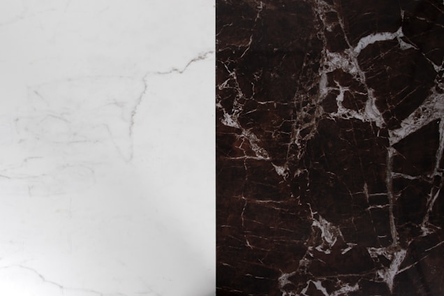 A surface divided into two contrasting marble textures, with the left side displaying a light-colored marble with subtle gray veining and the right side exhibiting a dark brown marble with prominent white veining.