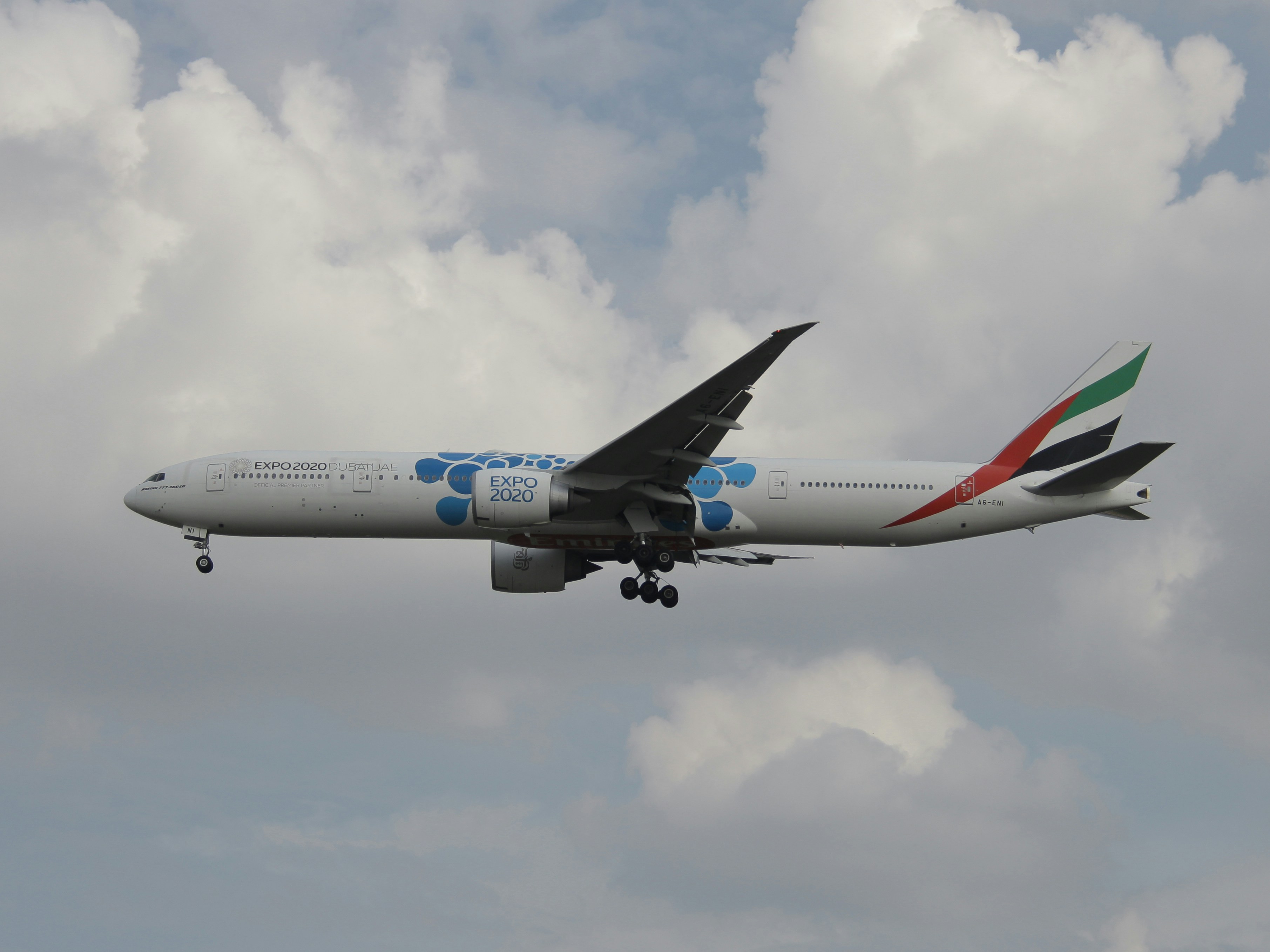 a large jetliner flying through a cloudy sky, Emirates Boeing 777-300ER Reg. A6-ENI (Dubai expo 2020 Livery)