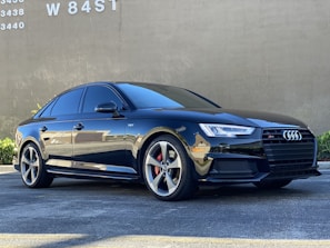 A polished Audi A4 parked beside a minimalist white wall with subtle shadows.