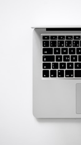 A minimalist image featuring the upper-left portion of a laptop keyboard against a plain white background. The keys are black with white symbols, and the laptop appears to have a silver or gray body.