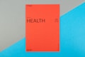 A vibrant red card with the word 'HEALTH' prominently displayed in black text, accompanied by smaller text indicating the number 09 (77) and phrases such as '77 HUMAN NEEDS' and '(physical)' at the top. The background consists of intersecting areas of blue and gray-green color.