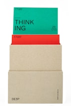 A beige box holds two cards. The top card is green with the word 'THINKING' prominently displayed in black text along with the phrase '(actional)' and other smaller text details. The card beneath is red, partially obscured by the green card, also containing textual information. The box has minimalistic text on its lower part.