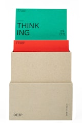 A beige box holds two cards. The top card is green with the word 'THINKING' prominently displayed in black text along with the phrase '(actional)' and other smaller text details. The card beneath is red, partially obscured by the green card, also containing textual information. The box has minimalistic text on its lower part.