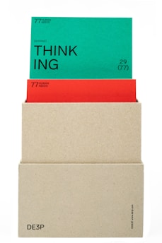 A beige box holds two cards. The top card is green with the word 'THINKING' prominently displayed in black text along with the phrase '(actional)' and other smaller text details. The card beneath is red, partially obscured by the green card, also containing textual information. The box has minimalistic text on its lower part.