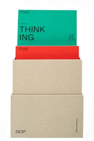 A beige box holds two cards. The top card is green with the word 'THINKING' prominently displayed in black text along with the phrase '(actional)' and other smaller text details. The card beneath is red, partially obscured by the green card, also containing textual information. The box has minimalistic text on its lower part.