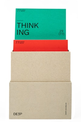 A beige box holds two cards. The top card is green with the word 'THINKING' prominently displayed in black text along with the phrase '(actional)' and other smaller text details. The card beneath is red, partially obscured by the green card, also containing textual information. The box has minimalistic text on its lower part.
