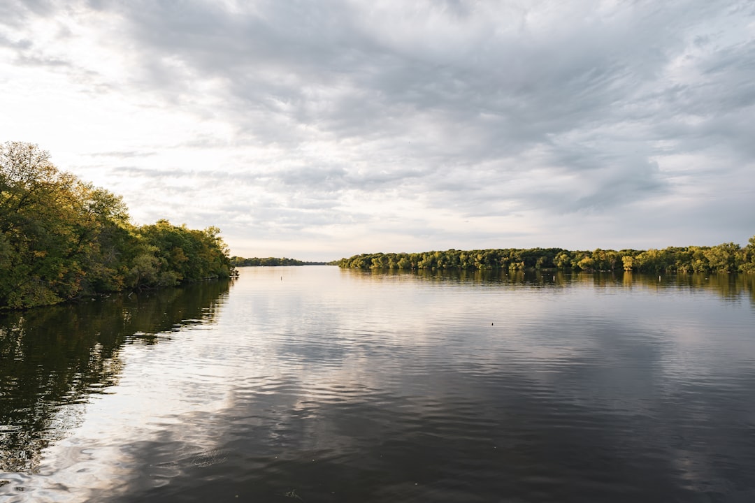 a body of water surrounded by trees under a cloudy sky, A view of the Mississippi River near Minneapolis