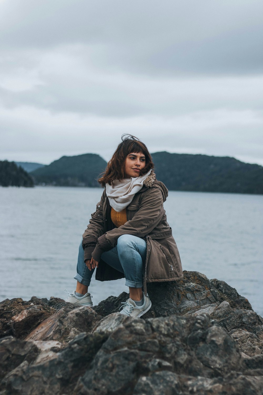 a woman is sitting on a rock by the water