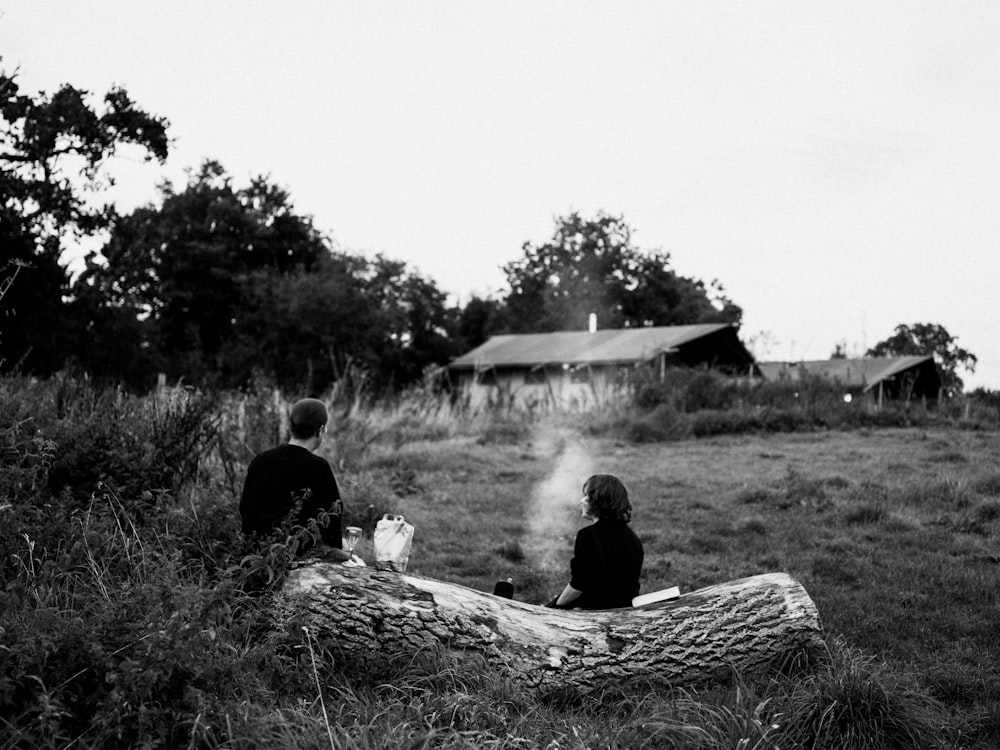 Zwei Personen sitzen auf einem Baumstamm auf einem Feld