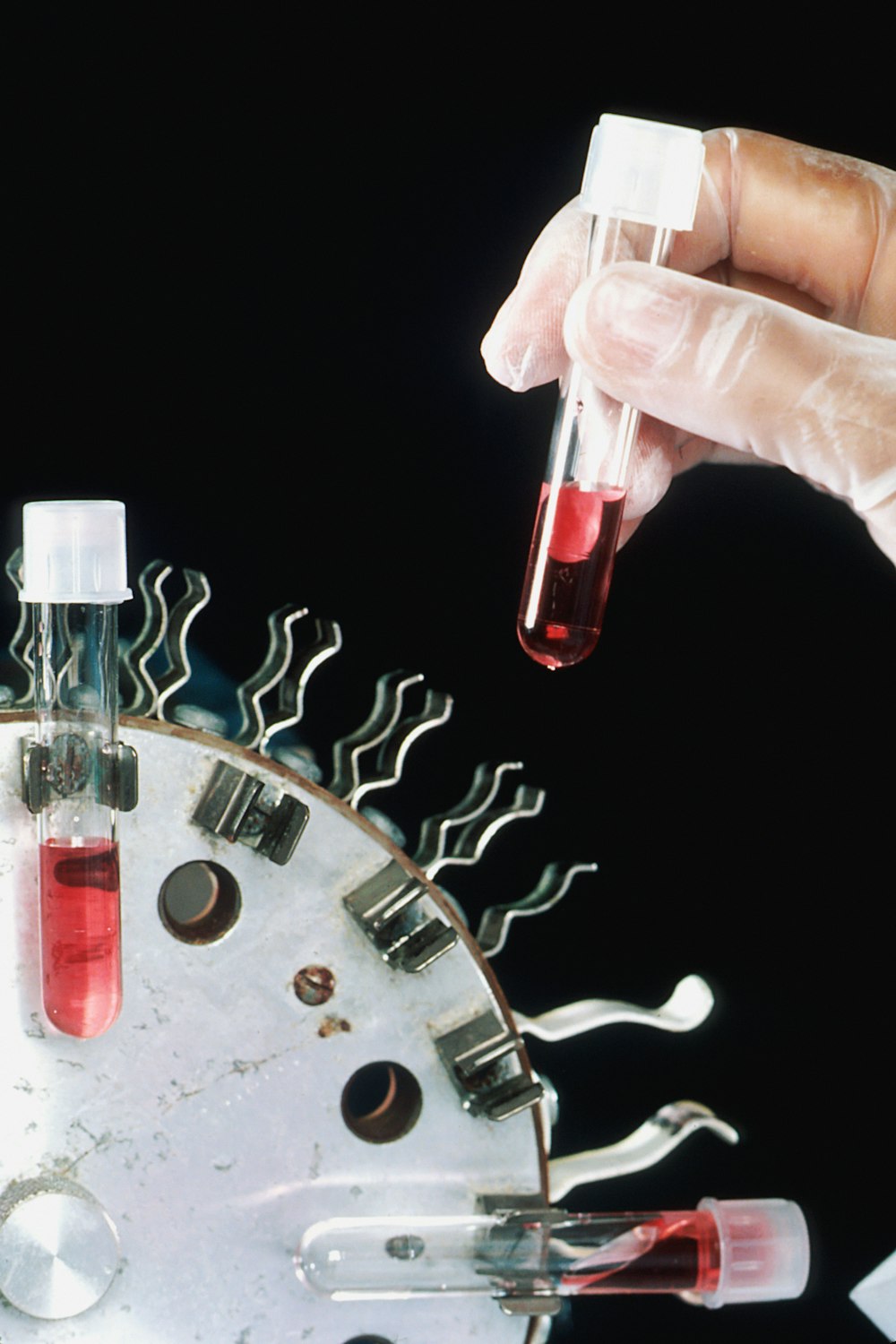 a person in white gloves is holding a test tube