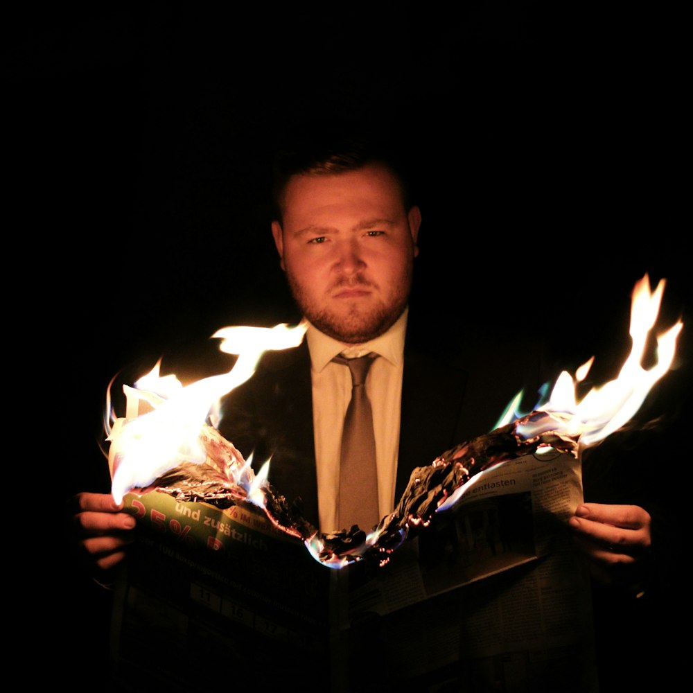 a man in a suit and tie holding a book with flames coming out of it