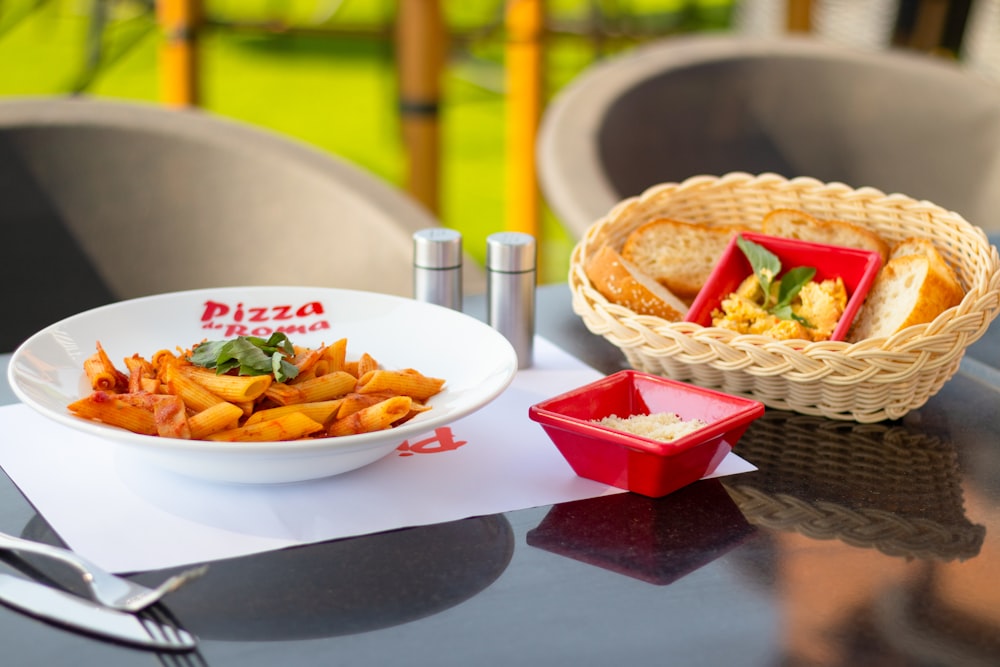 a table with a bowl of pasta and a basket of bread