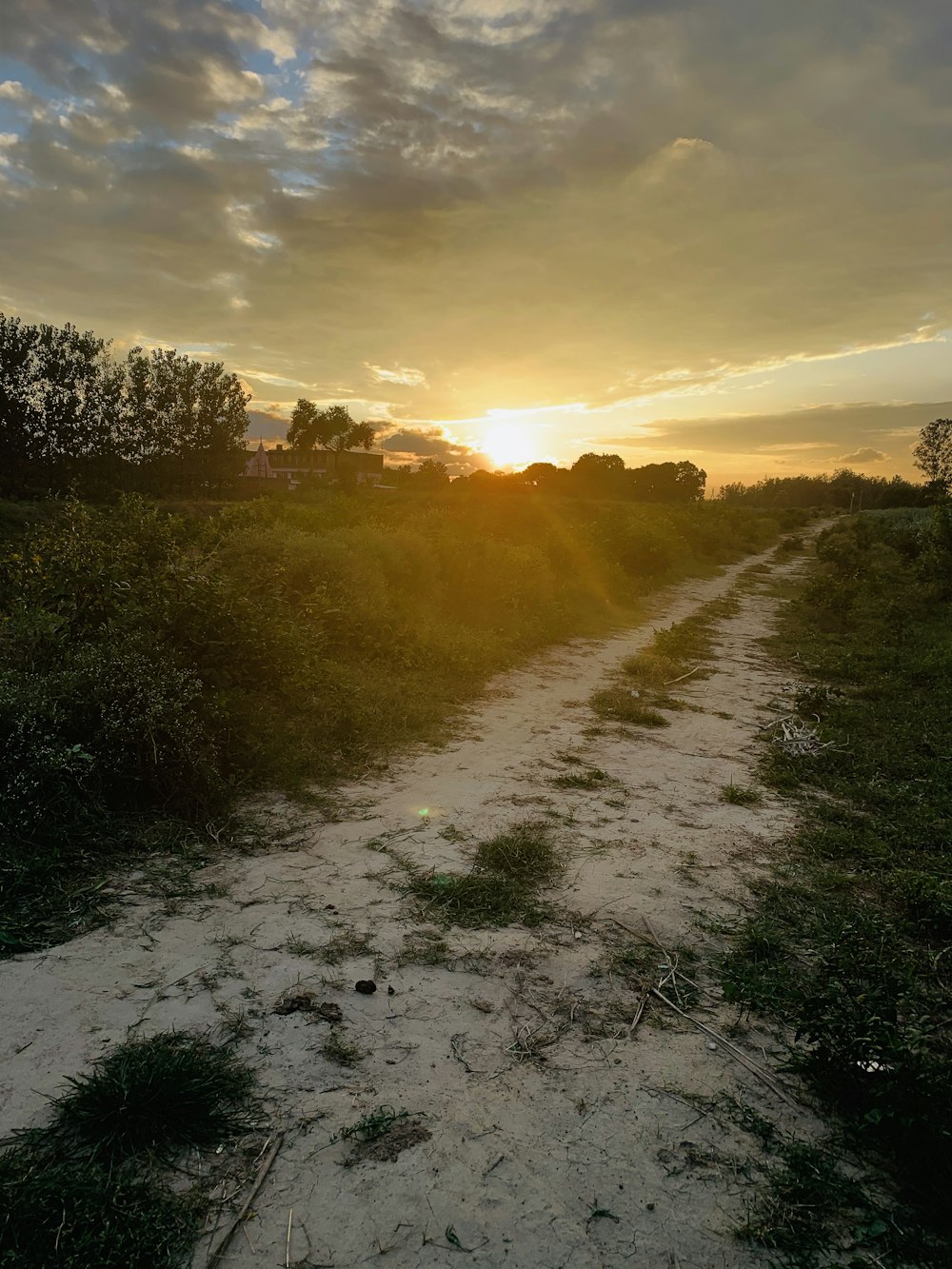 the sun is setting over a dirt road