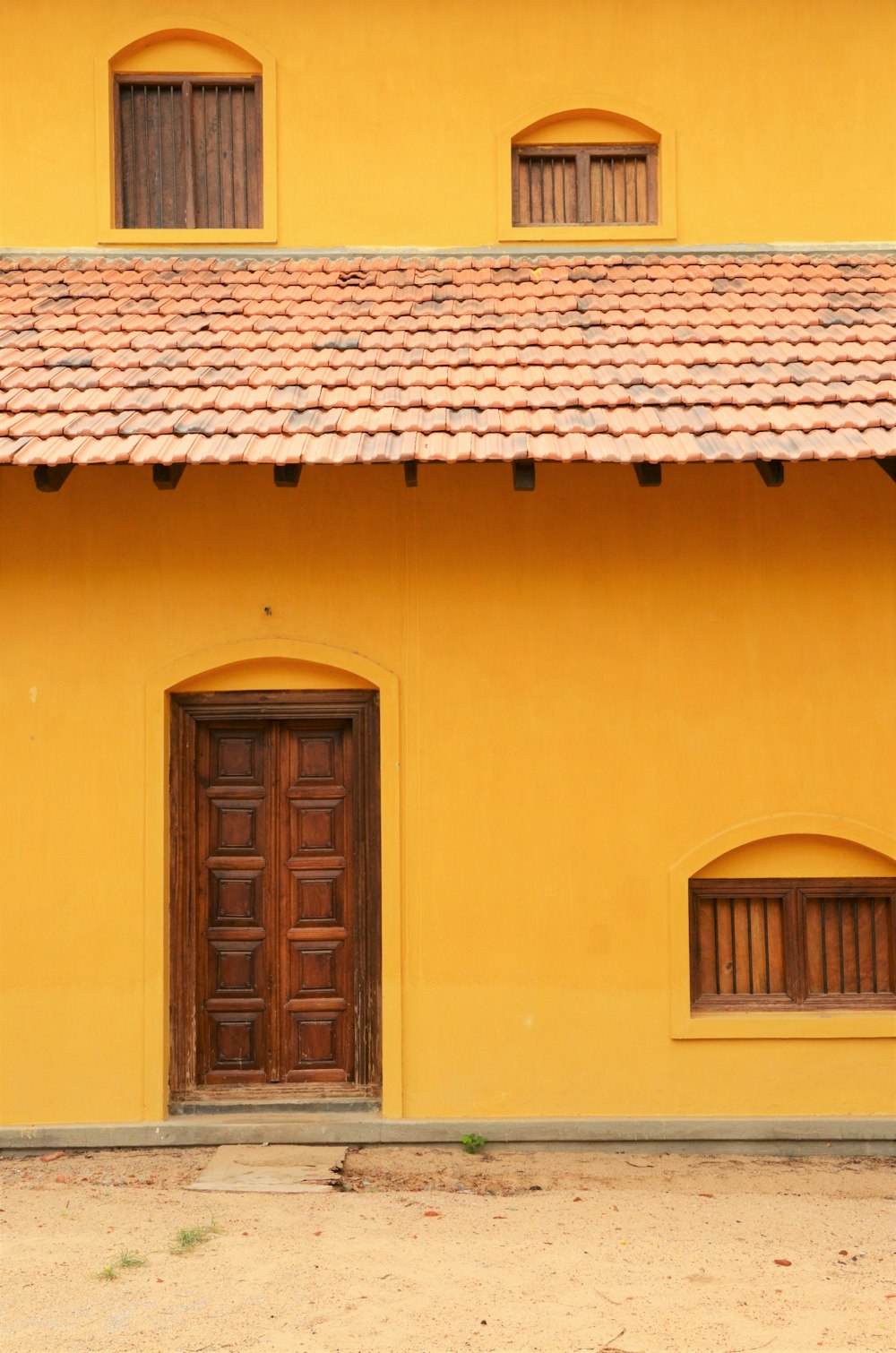 a yellow building with two brown doors and two windows
