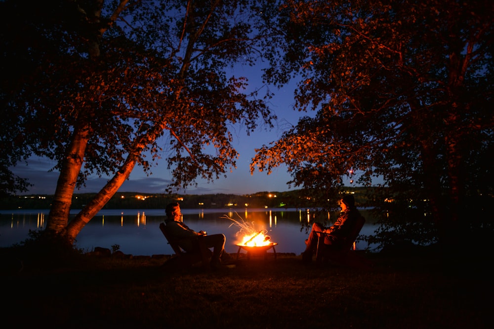 two people sitting around a campfire at night