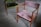A pair of vintage wooden chairs with plush upholstery are placed on a smooth, grey concrete floor. One chair features a muted pink fabric, while the other has a rich green covering. The chairs have a minimalist, mid-century design with angular armrests and simple frames.
