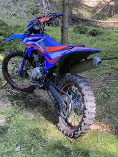 Side view of a vibrant red electric dirt bike parked against a forest backdrop.