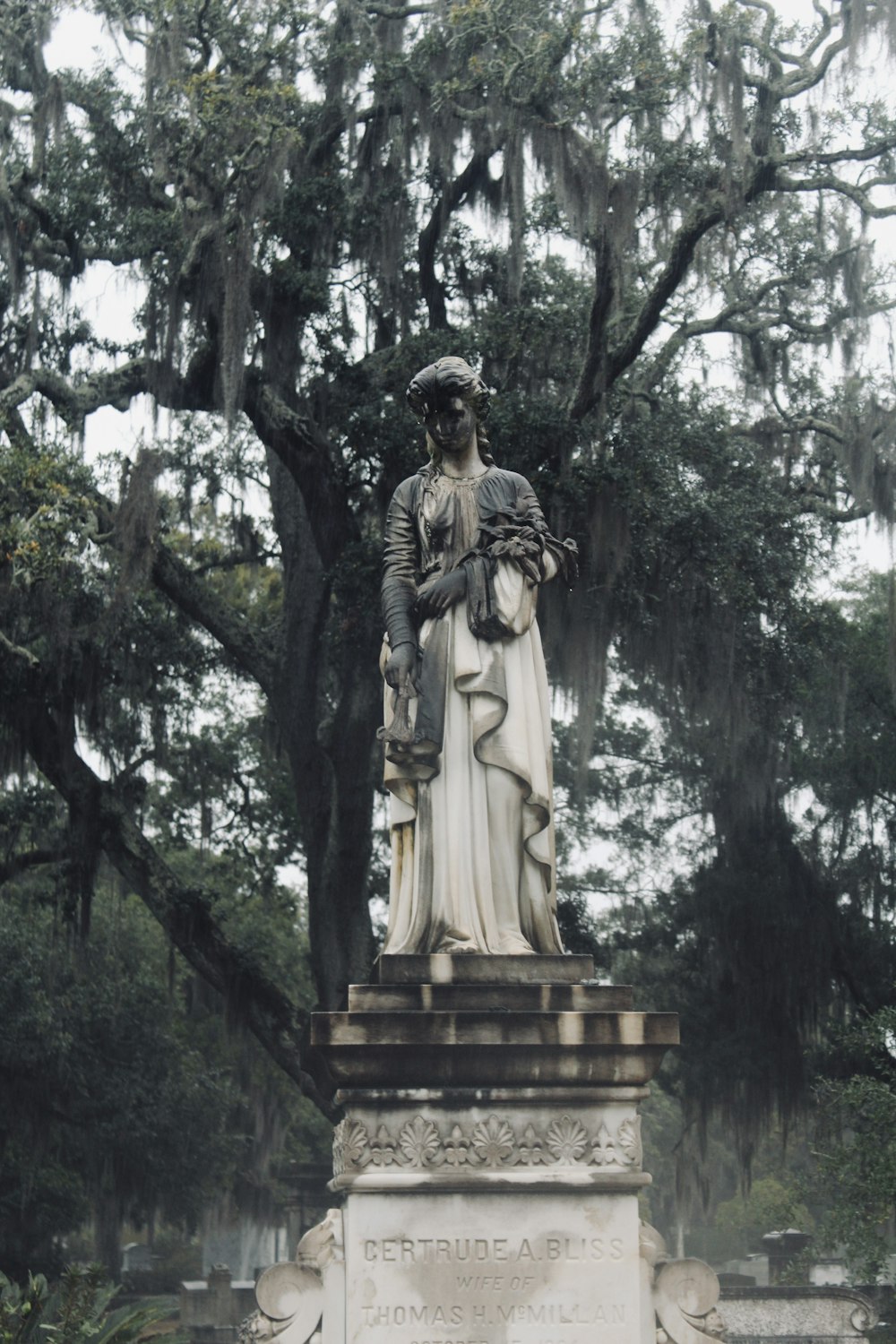 a statue of a woman standing in front of a tree