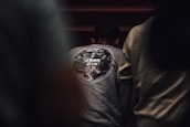 A person is wearing a gray sweatshirt with a design of the Earth on the back, along with the text 'John 3:16.' The surrounding environment is dimly lit, creating a focused atmosphere.