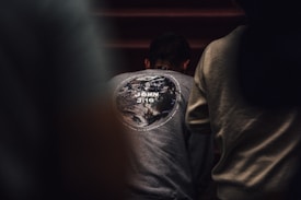 A person is wearing a gray sweatshirt with a design of the Earth on the back, along with the text 'John 3:16.' The surrounding environment is dimly lit, creating a focused atmosphere.