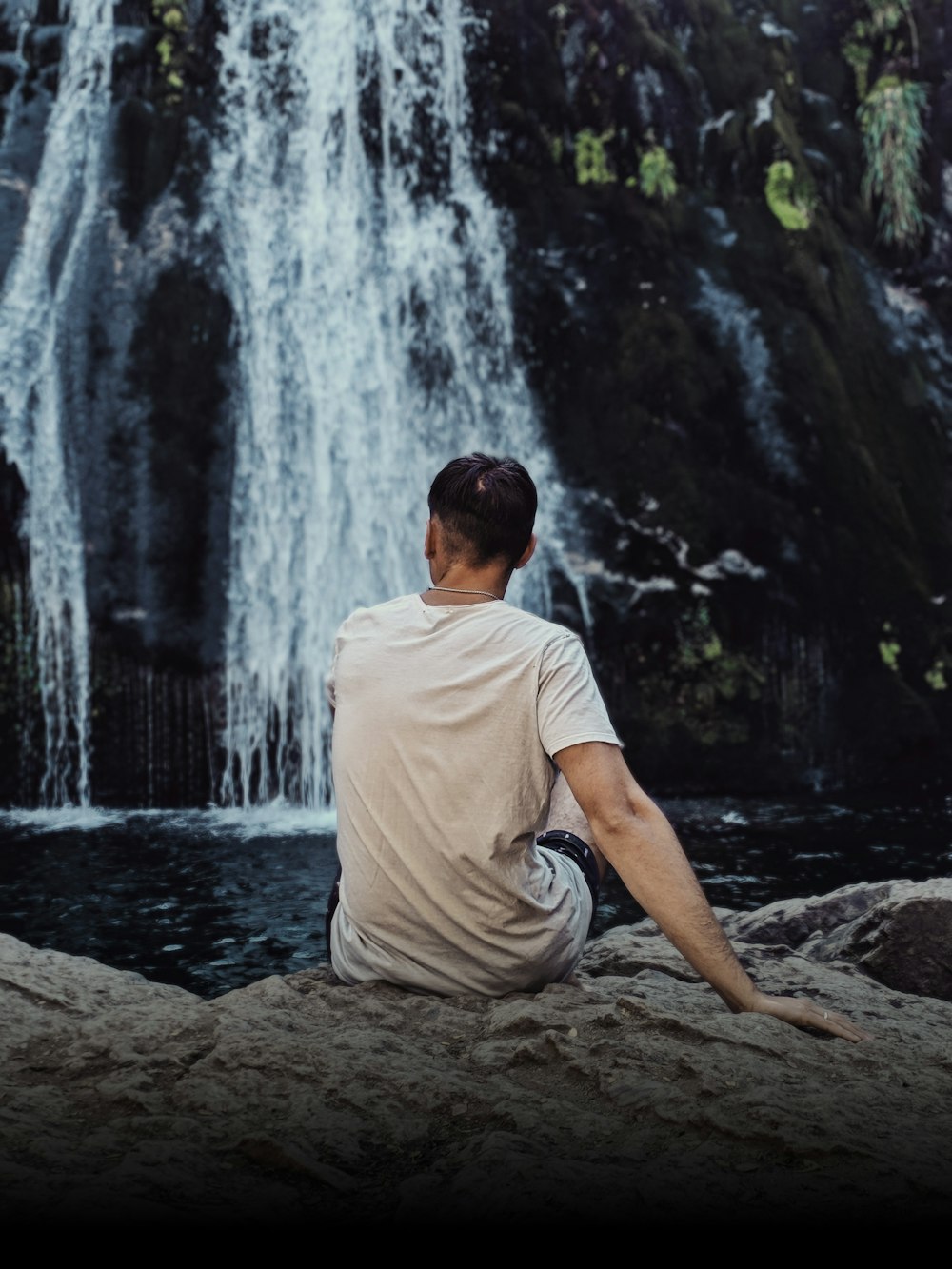 a man sitting on a rock in front of a waterfall