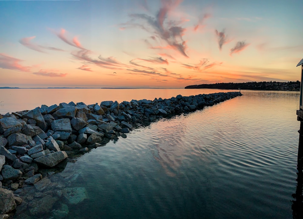 a dock with rocks in the water and a sunset in the background