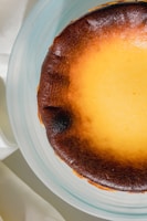 Close-up of a creamy basque cheesecake with a golden-brown top and a few fresh green leaves on the side.