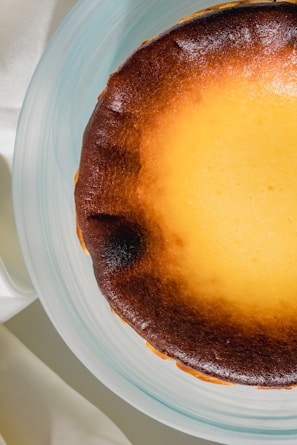 Close-up of a creamy basque cheesecake with a golden-brown top and a few fresh green leaves on the side.