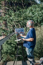 A warm portrait of Super Mattie painting outdoors surrounded by lush greenery and friendly animals.