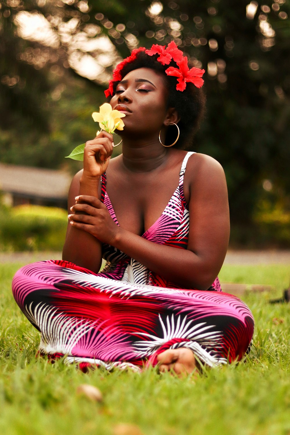 a woman sitting in the grass with a flower in her mouth