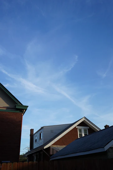 A freshly shingled roof on a suburban home under a clear blue sky.