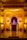 An ornate stage decorated with intricate carvings and arches, illuminated by warm yellow lighting. At the center of the stage is a small idol of Lord Ganesha, adorned with garlands and surrounded by religious offerings.