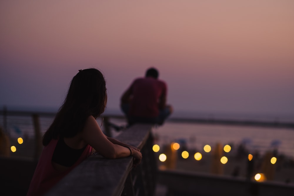 a man and a woman sitting on a pier watching the sunset