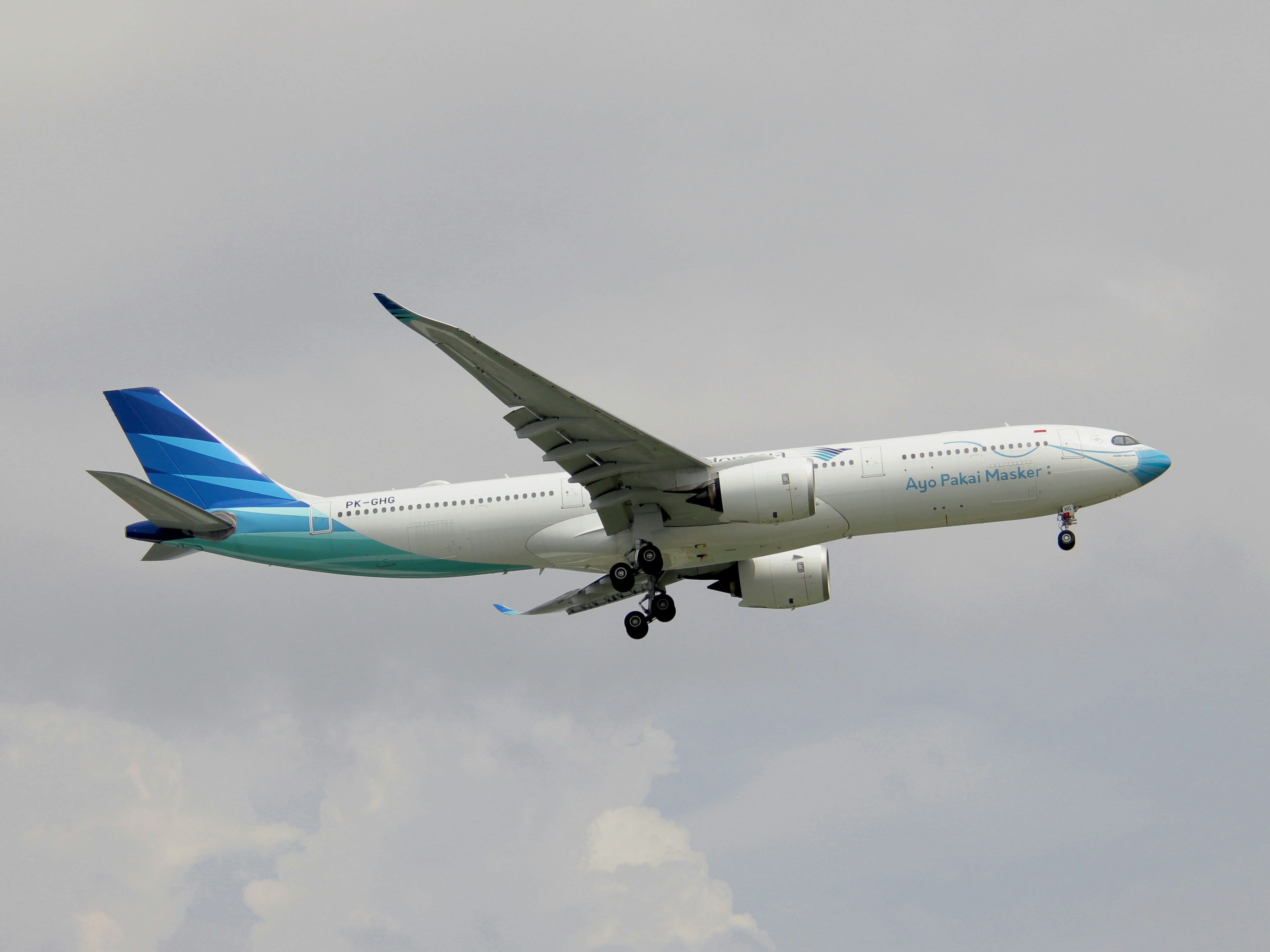 a large jetliner flying through a cloudy sky, Garuda Indonesia A330-900Neo</p><p>PK-GHG (Ayo pakai masker Livery)