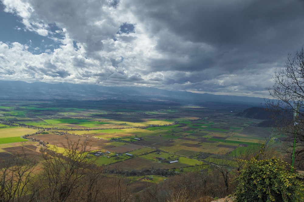 a scenic view of a valley with green fields under a cloudy sky