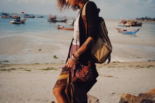 a woman walking on the beach carrying a purse