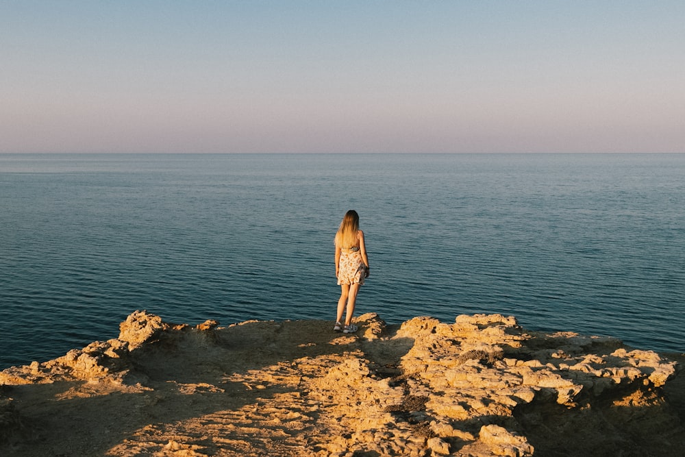 a woman standing on top of a rocky cliff next to the ocean