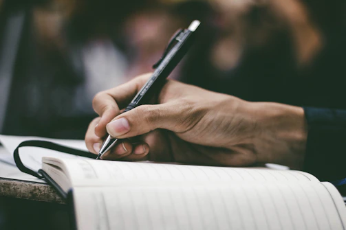 Close-up of a student’s hands holding a notebook and pen during class.
