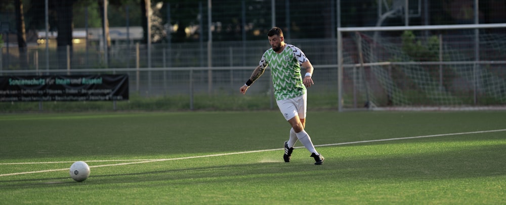 um homem em um uniforme verde e branco chutando uma bola de futebol