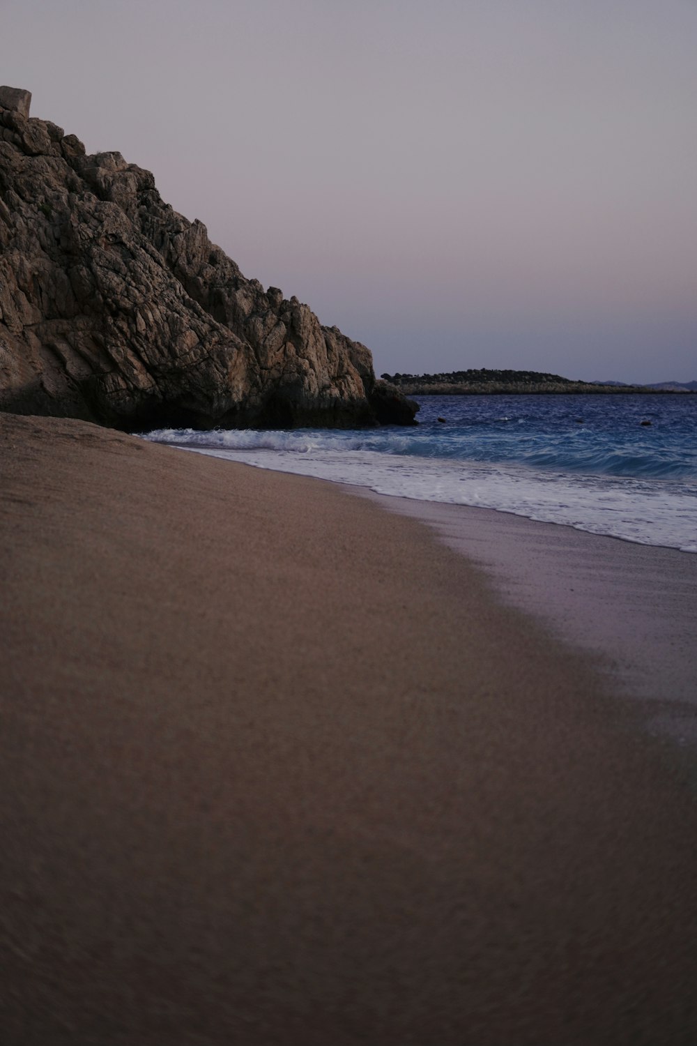 a beach with waves coming in to the shore and a rock outcropping