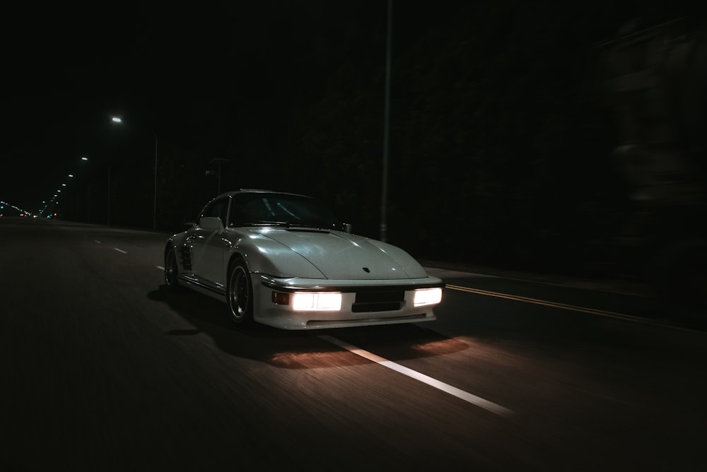 a white sports car driving down a street at night