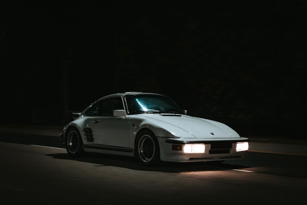 a white car driving down a street at night