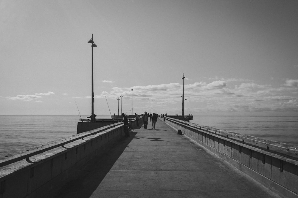a black and white photo of people walking on a pier