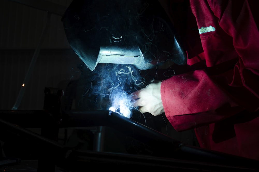 a person in a red jacket working on a piece of metal
