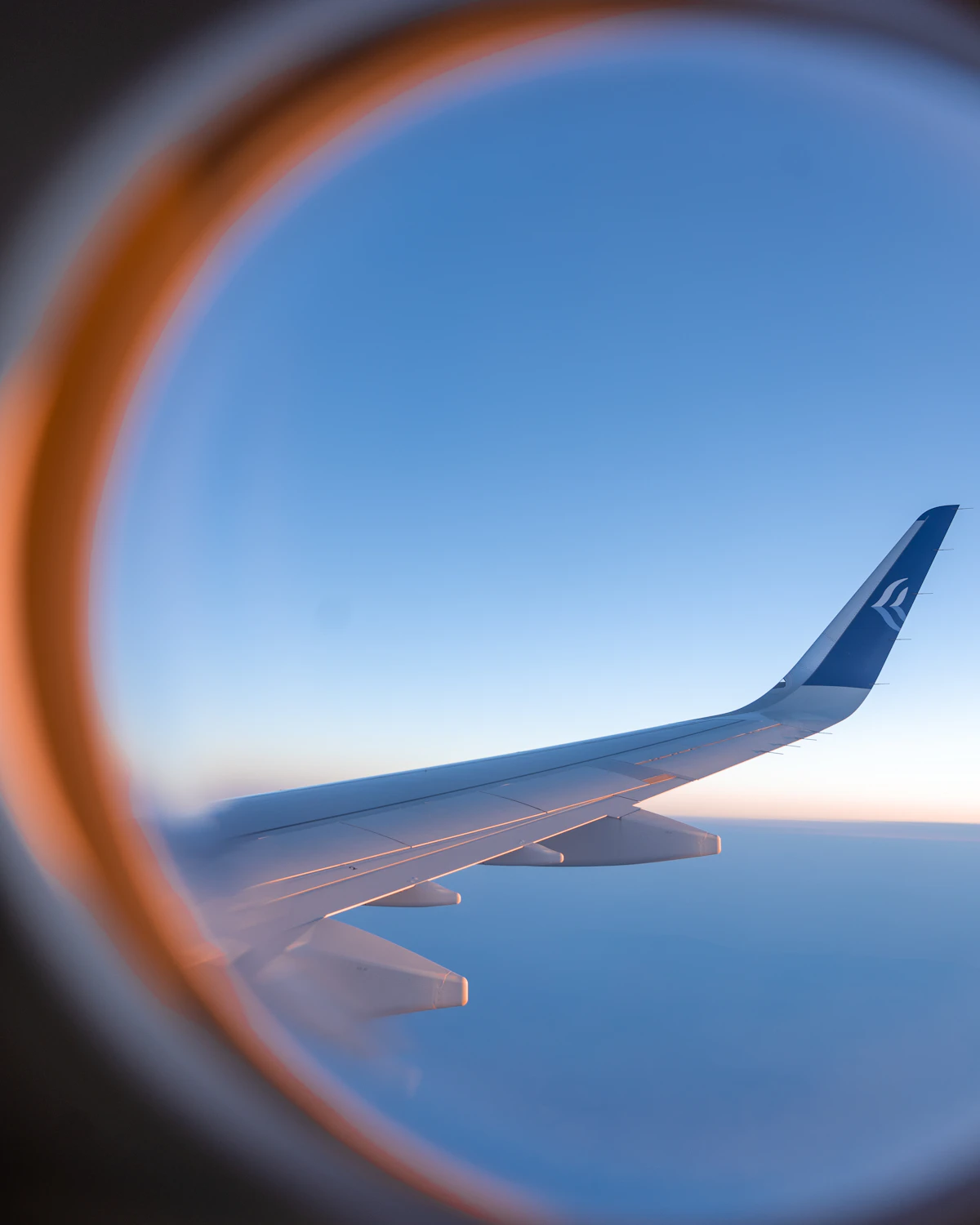 View of an airplane wing through a cabin window above the clouds