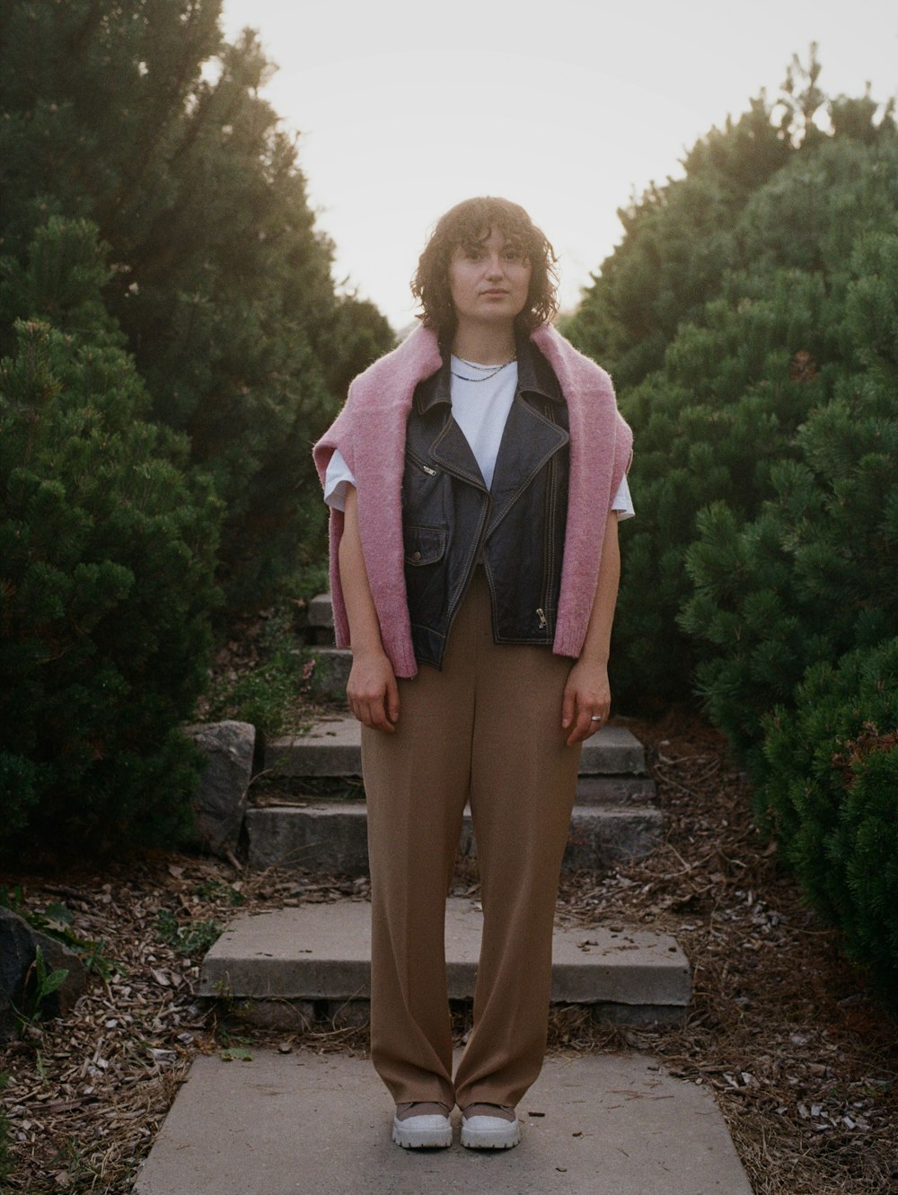 a woman standing on a path in front of bushes